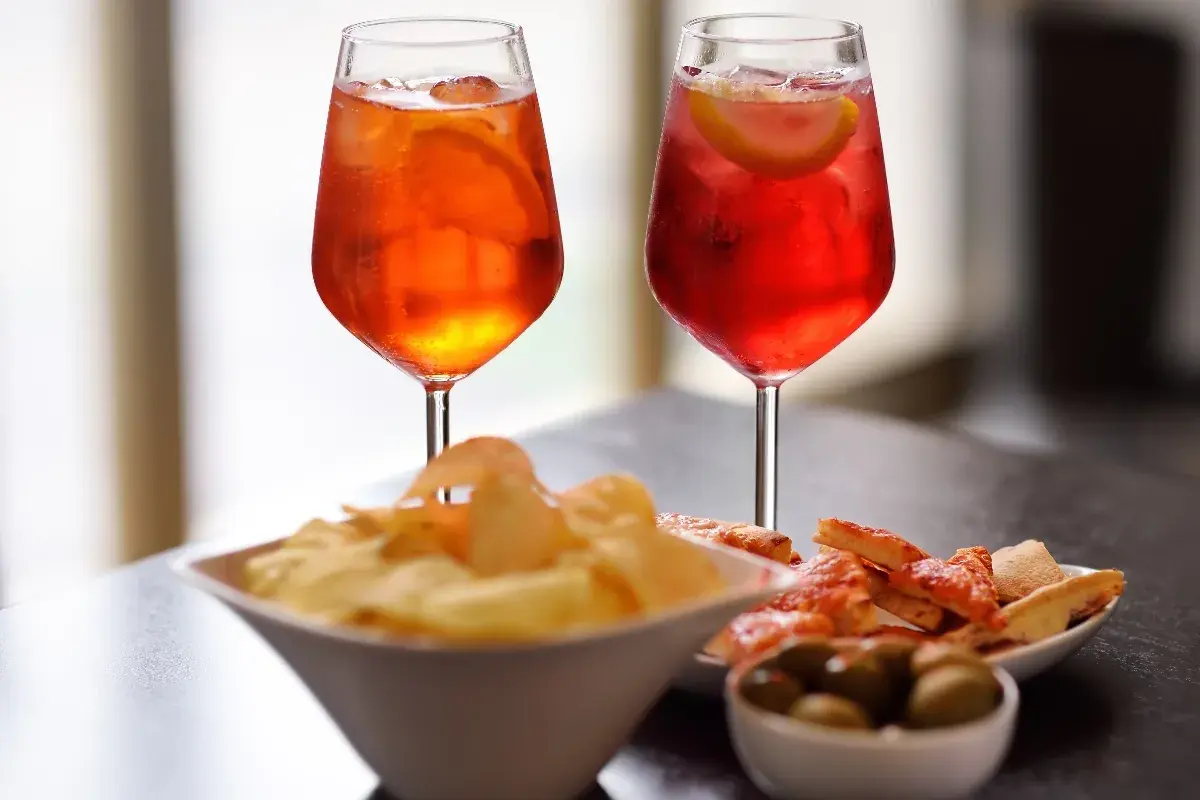 Due cocktail colorati, patatine, olive e pizzette per un romantico aperitivo serale.