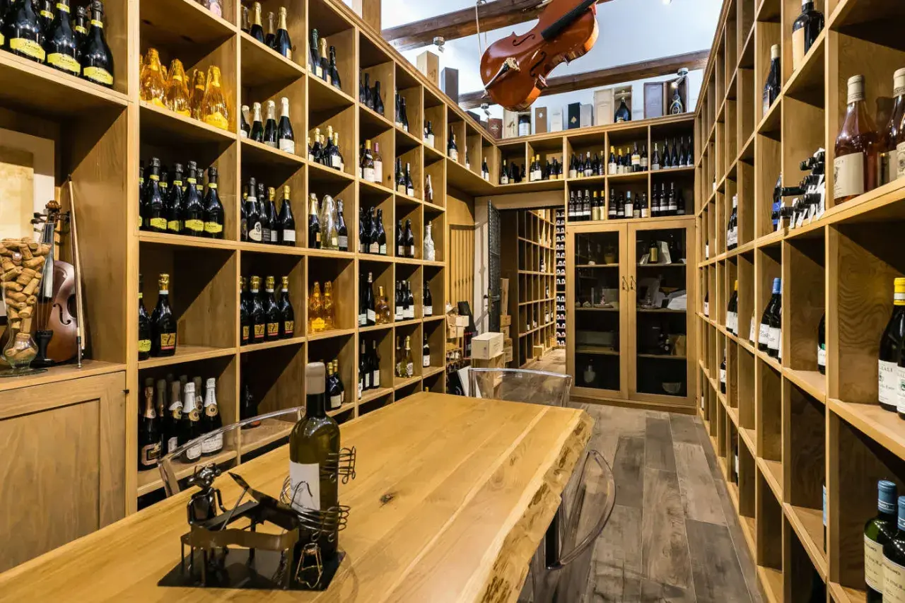 Cantine siciliane con scaffalature in legno piene di bottiglie di vino, un violino appeso e un tavolo in legno massiccio.