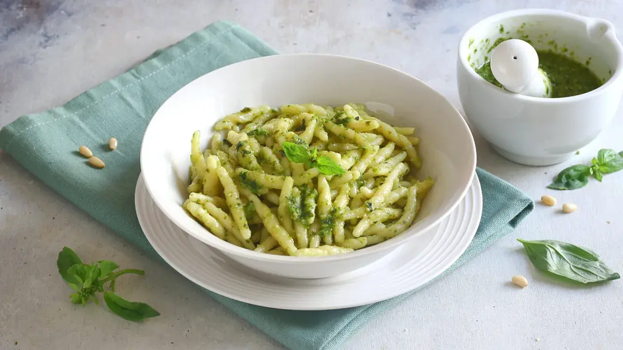 Piatto di trofie al pesto, con mortaio e basilico. Un'idea su cosa abbinare alla pasta al pesto per un pasto fresco e gustoso.