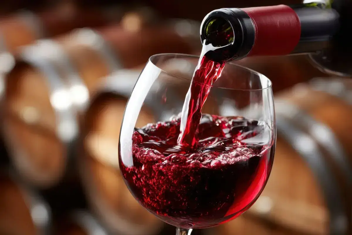 Versando vino rosso in un calice, con botti di legno sullo sfondo. Un sorso di il dolcetto.