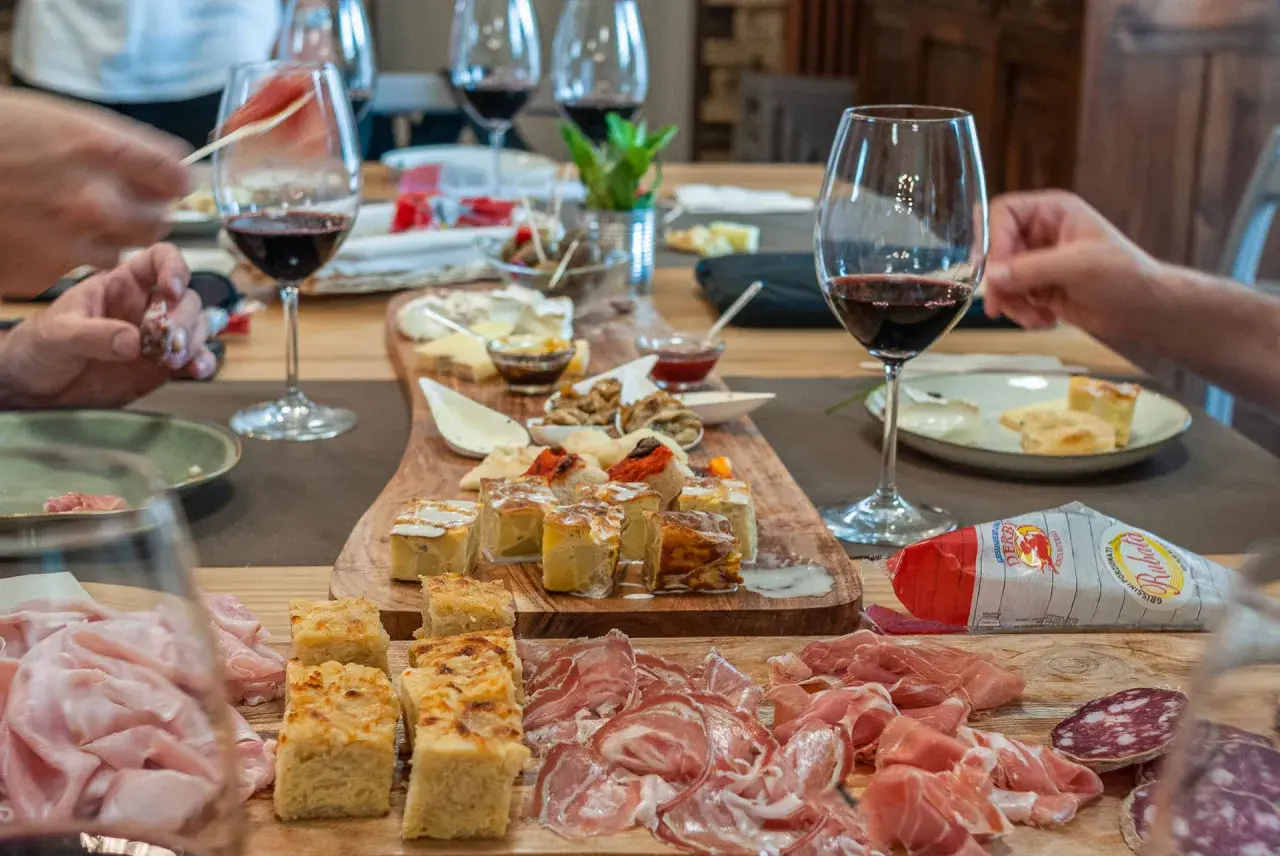 Un tavolo imbandito per una degustazione enogastronomica: salumi, formaggi, focacce e vino rosso invitano a un'esperienza di sapori.