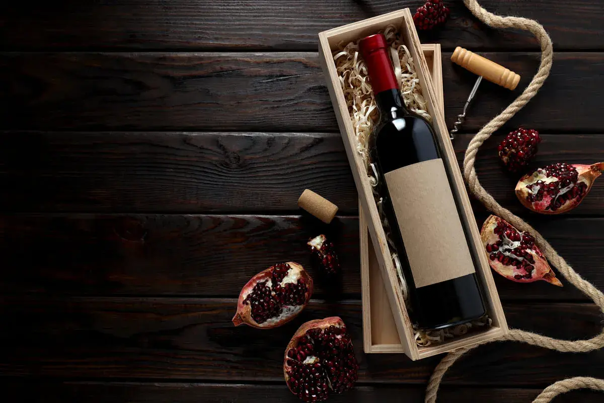 Scatola di legno con bottiglia di vino rosso, melograni e cavatappi, evocando i vini tipici della Campania.