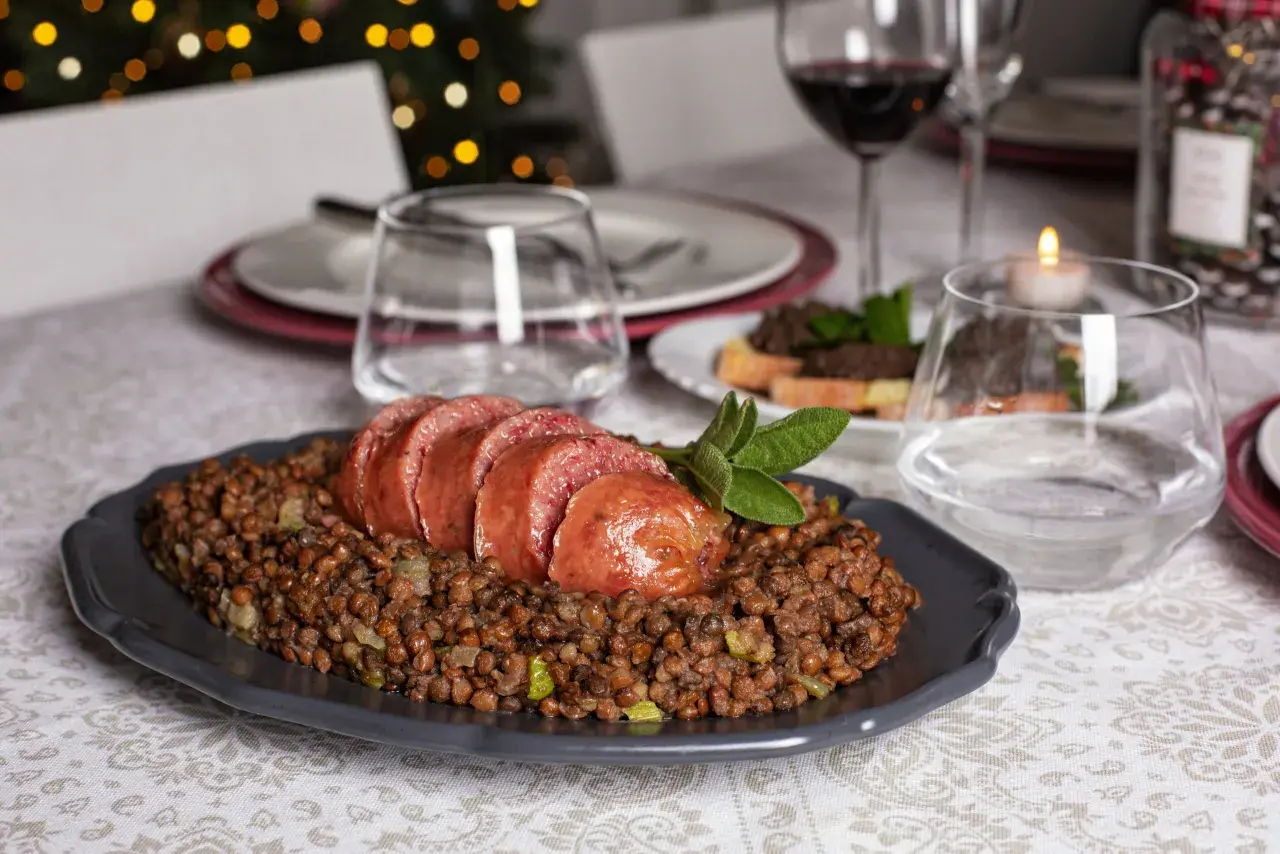 Piatto di cotechino affettato su lenticchie, pronto per essere gustato con un buon vino da abbinare al cotechino.