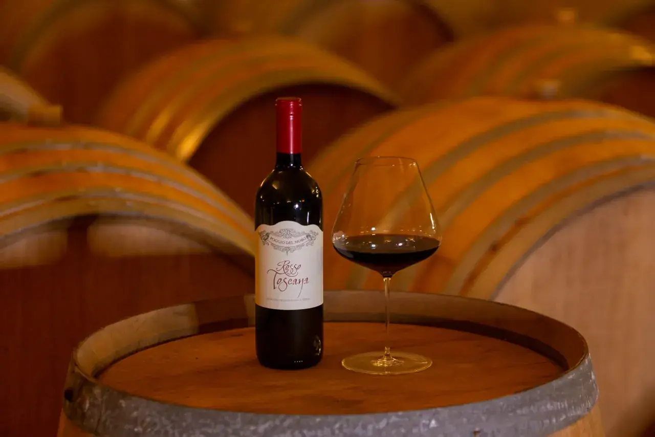 Bottiglia e calice di vino rosso su una botte, con botti di legno sullo sfondo. Un assaggio del governo toscano vino.