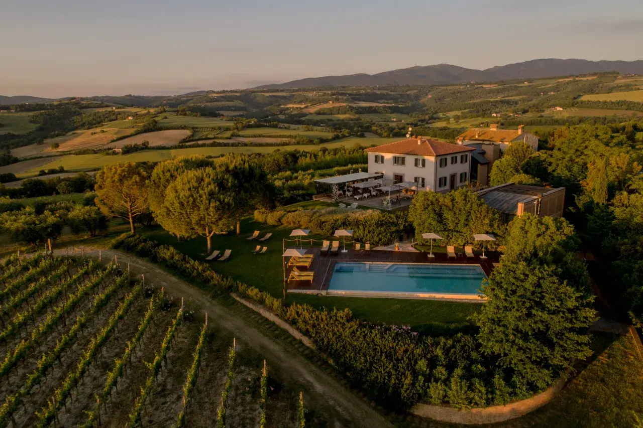 Un incantevole wine resort in Umbria, con vigneti rigogliosi, una piscina scintillante e colline ondulate al tramonto.
