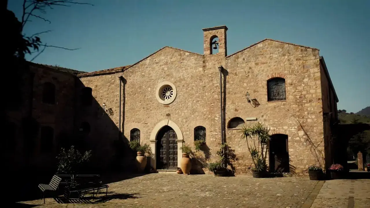 L'abbazia Santa Anastasia, con la sua facciata in pietra e il campanile, si affaccia su un cortile acciottolato.