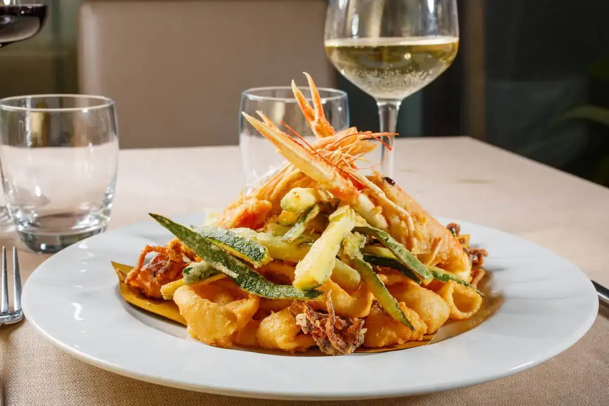 Un piatto invitante di fritto misto di mare, con gamberi e calamari croccanti, accompagnato da verdure fritte e un bicchiere di vino per frittura di pesce.