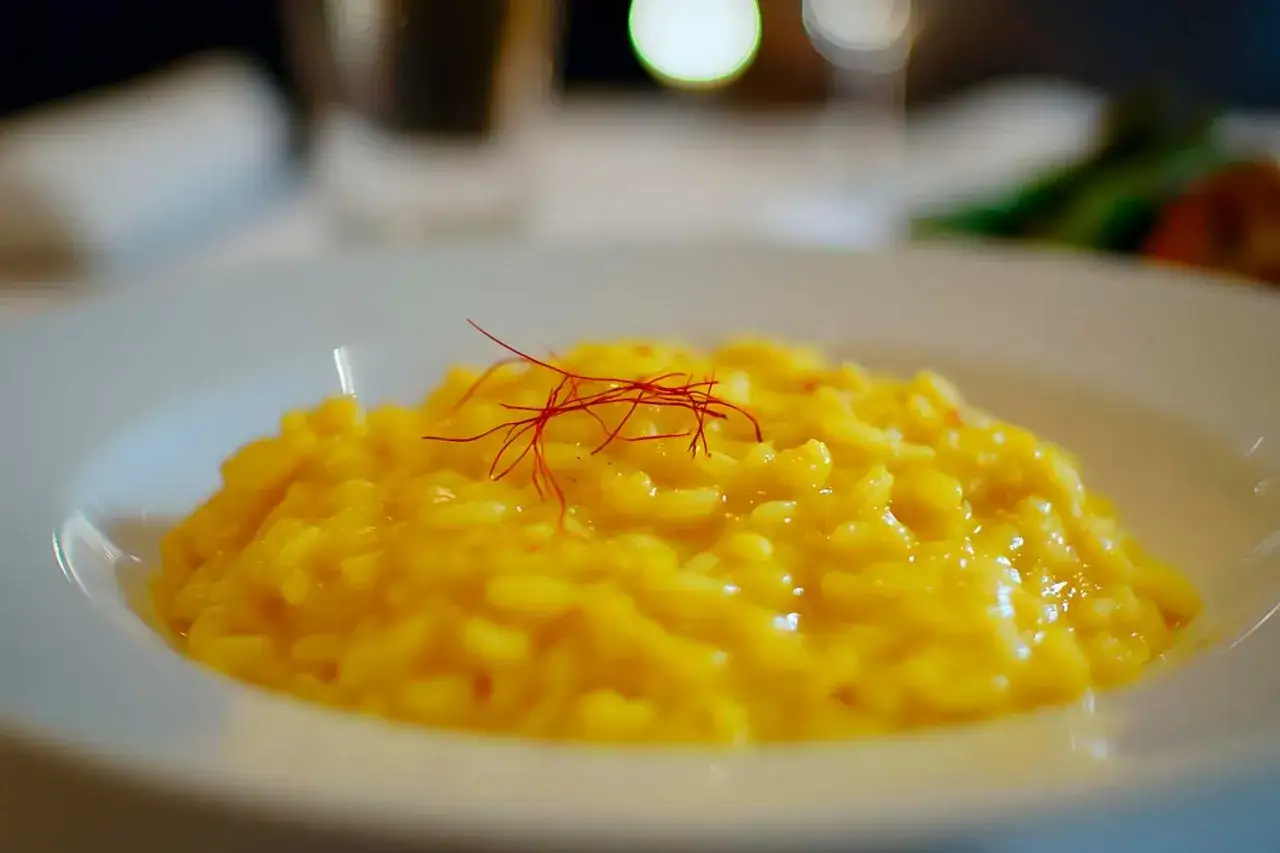 Risotto allo zafferano cremoso, guarnito con fili rossi. Un perfetto abbinamento vino risotto zafferano per un'esperienza culinaria indimenticabile.