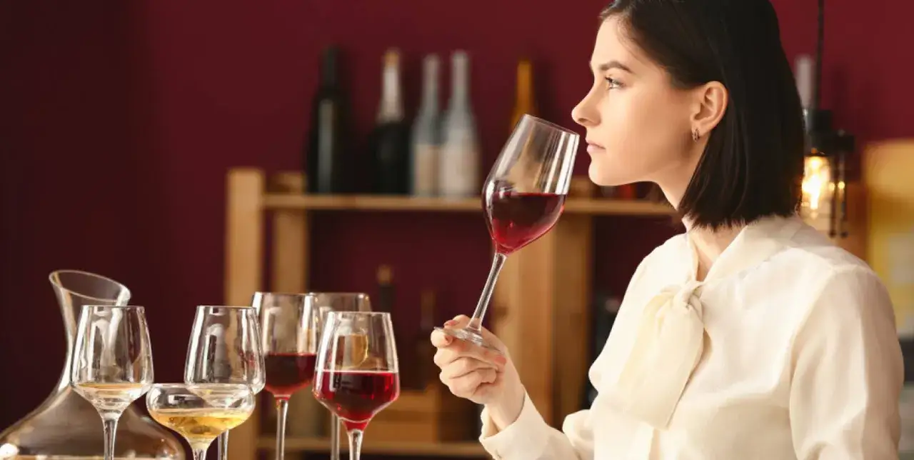 Donna annusa un bicchiere di vino rosso, parte di una degustazione. Il vero significato di degustazione è apprezzare ogni sfumatura.