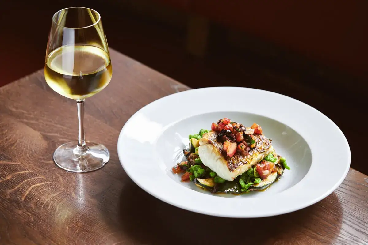 Piatto di pesce con verdure e un bicchiere di vino bianco, perfetti abbinamenti per una Ribolla Gialla.