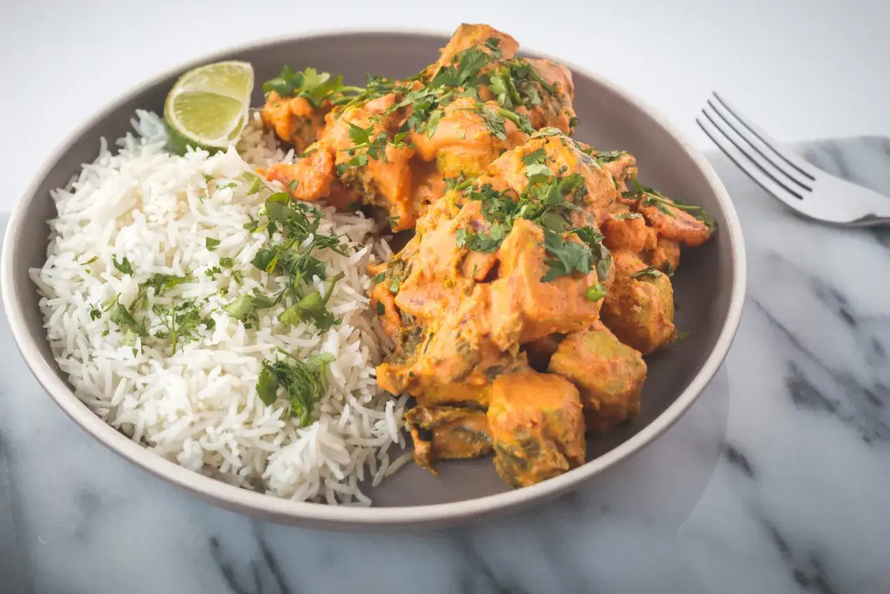 Piatto di riso basmati con pollo al curry cremoso e coriandolo fresco. Un lime a spicchio completa il piatto, perfetto come vino da abbinare al pollo al curry.
