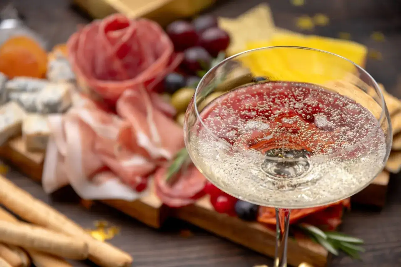 Un bicchiere di vino frizzante, pronto per chiacchiere e vino con un tagliere di salumi, formaggi e uva.