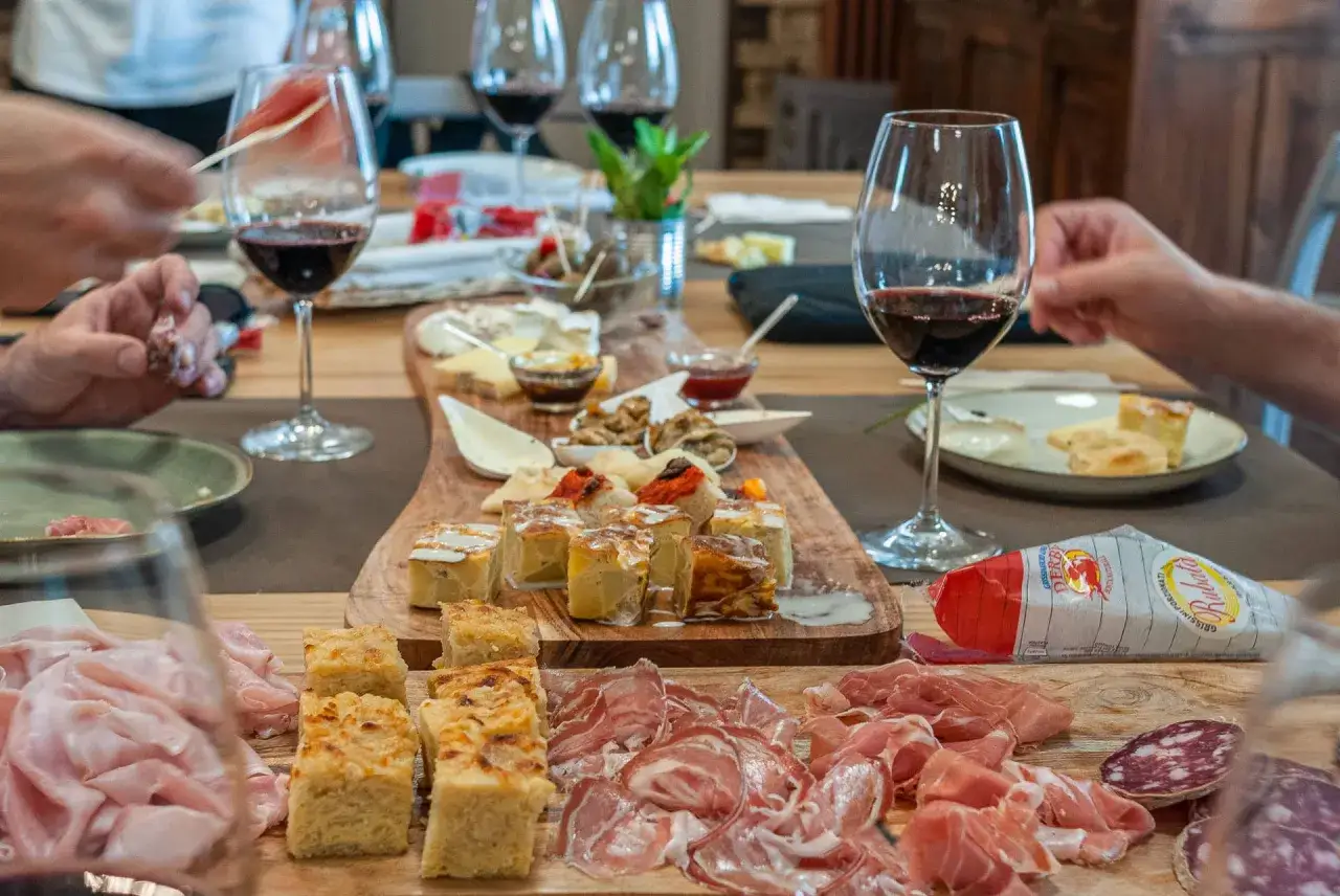 Un tavolo imbandito per una degustazione enogastronomica: salumi, formaggi, focacce e vino rosso invitano a un'esperienza di sapori.