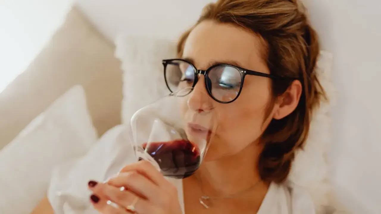 Donna con occhiali sorseggia vino rosso, apprezzandone il gusto tannico.