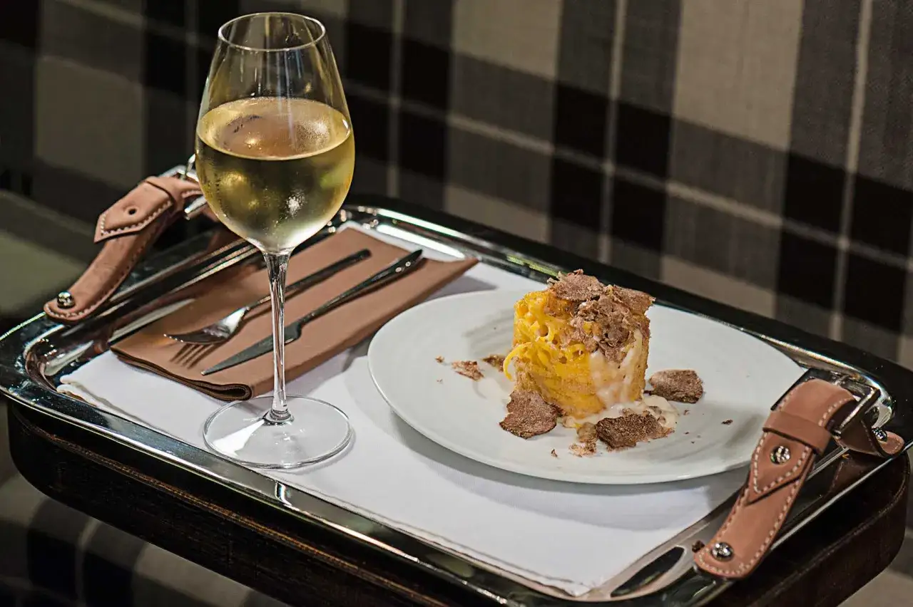 Un bicchiere di vino bianco, perfetto vino da abbinare al tartufo bianco, accanto a un piatto di pasta con abbondante tartufo grattugiato.