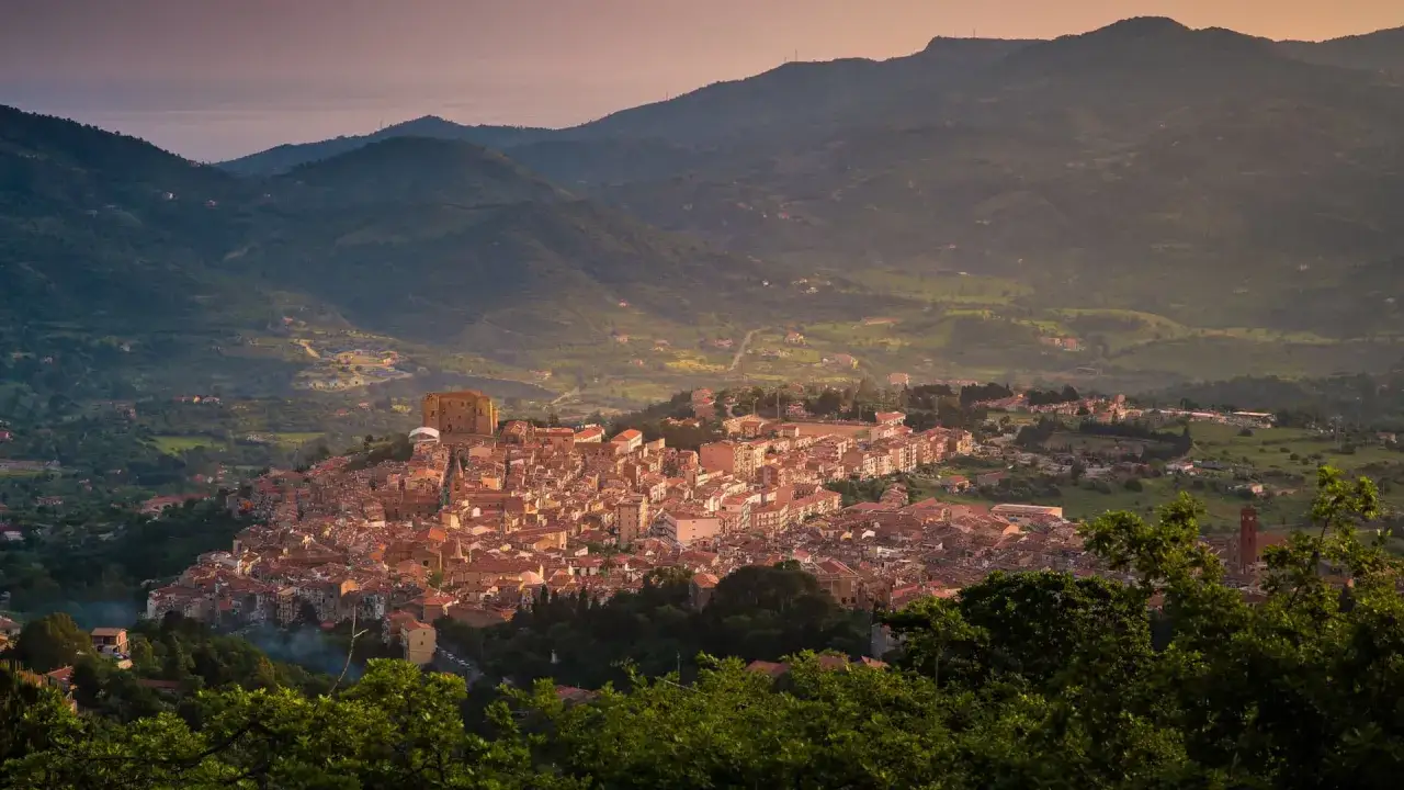Vista panoramica di un borgo collinare con tetti rossi, dominato da un castello. Si intravede la torre campanaria della chiesa di Santa Anastasia.