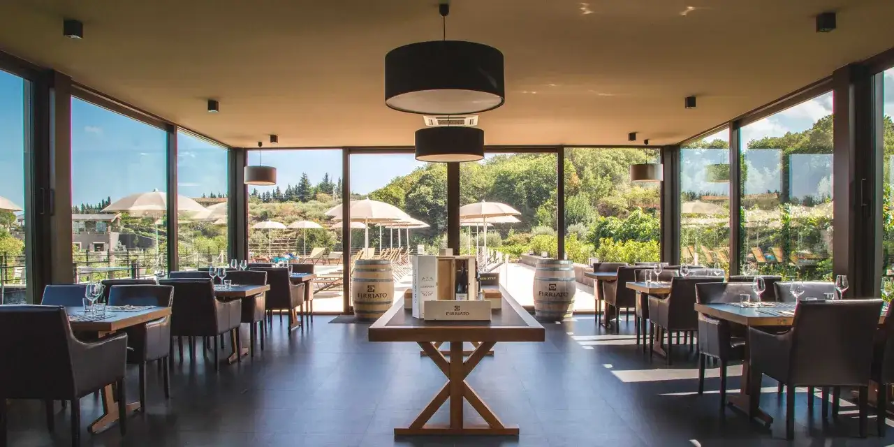 Sala degustazione con tavoli apparecchiati e vista su vigneti, ideale per un tour cantine Sicilia.