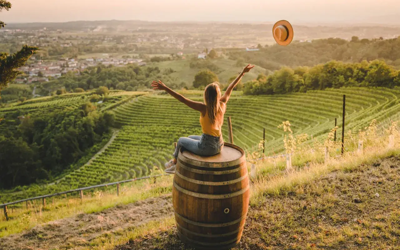 Donna su botte di legno ammira i vigneti delle cantine Friuli Venezia Giulia al tramonto.