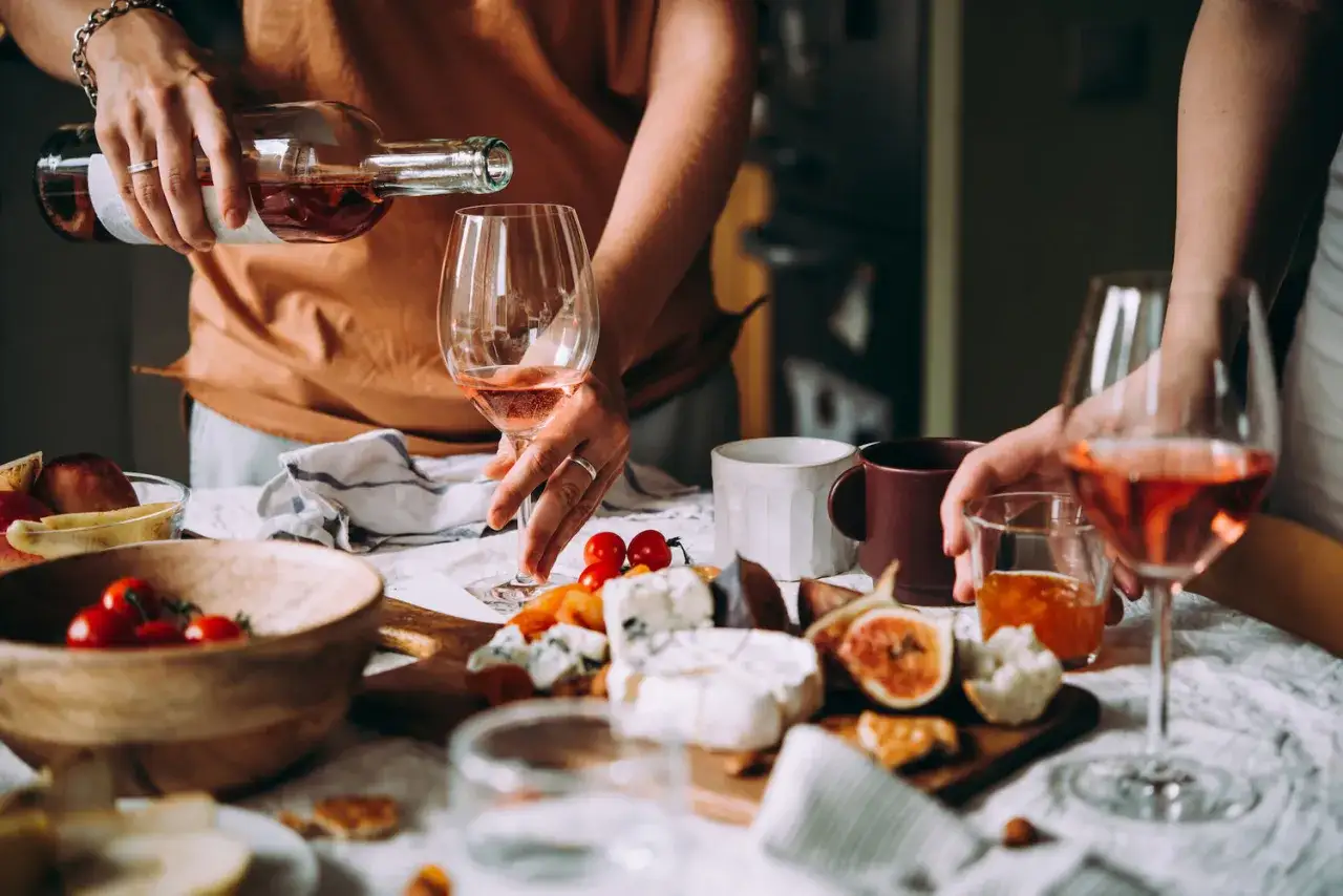Un bicchiere di vino rosato viene versato su un tagliere con formaggi, fichi e pomodorini. Esempi di food pairing per un aperitivo.