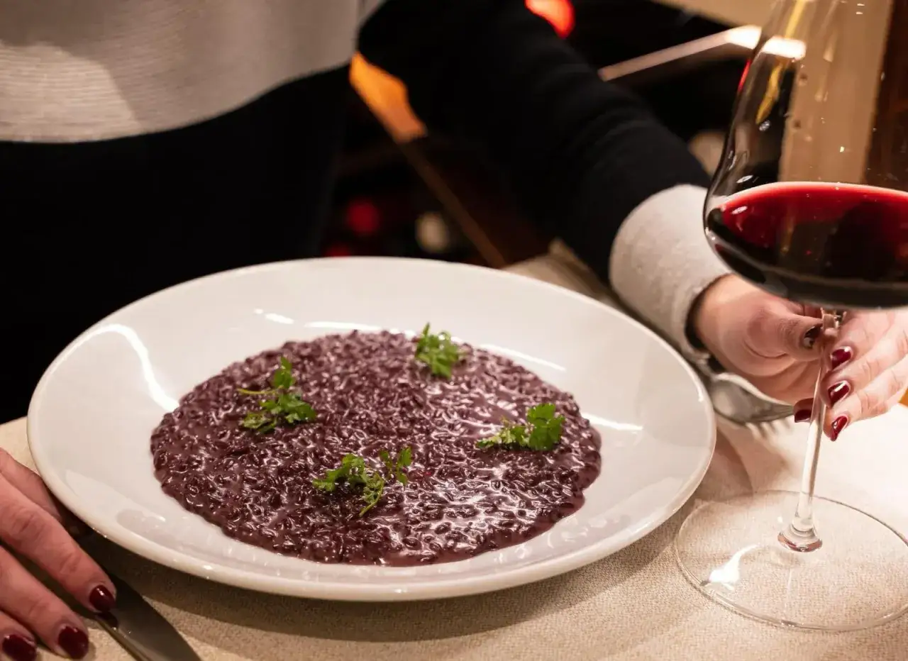 Risotto viola con prezzemolo, perfetto per gli amarone abbinamenti. Un bicchiere di vino rosso completa la scena.