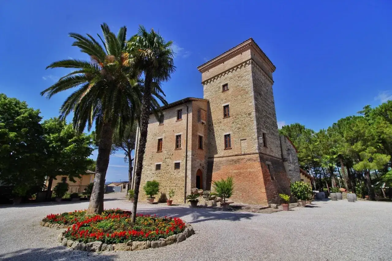 Le cantine Goretti, un'antica torre in pietra e mattoni, circondata da palme e fiori, sotto un cielo azzurro.