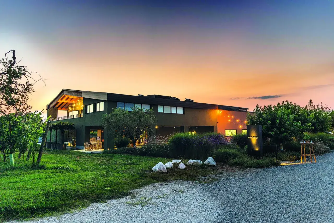 La cantina Ca' Maiol, illuminata al tramonto, accoglie con un'atmosfera magica. Vigneti e un giardino curato circondano la struttura moderna.