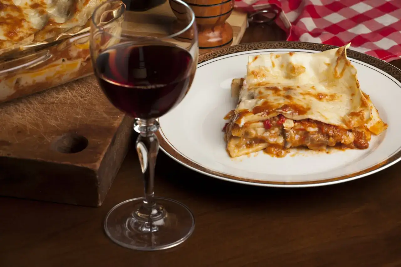 Un bicchiere di vino rosso accompagna una porzione di lasagna fumante, un abbinamento perfetto per un pasto delizioso.