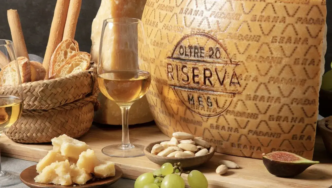 Un bicchiere di vino bianco accompagna un pezzo di Grana Padano Riserva, pane, uva e fichi.