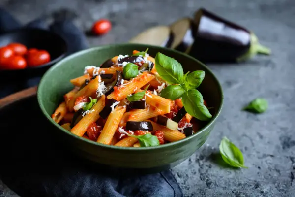 Piatto di pasta alla norma con melanzane, pomodoro e basilico, perfetto per un abbinamento vino.
