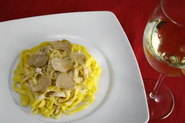 Tagliatelle con crema e scaglie di tartufo bianco, accanto un calice di vino da abbinare al tartufo bianco.