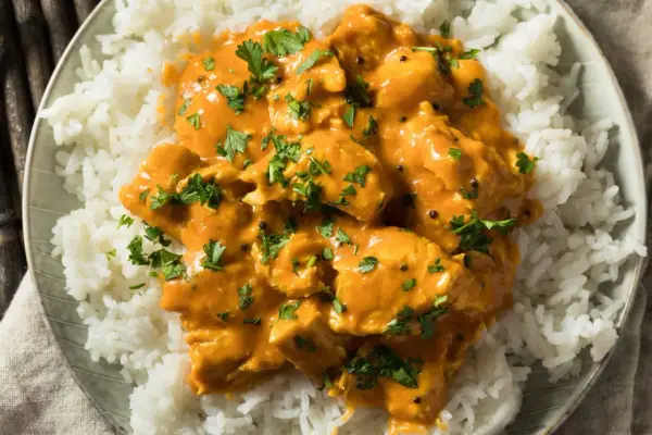 Pollo al curry cremoso su riso bianco, guarnito con prezzemolo fresco. Un vino da abbinare al pollo al curry? Un Gewürztraminer o un Riesling.
