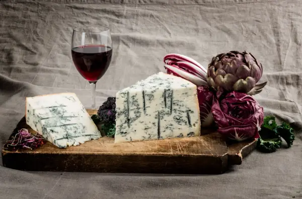 Gorgonzola e vino rosso su tagliere rustico, con radicchio e carciofo. Un perfetto gorgonzola abbinamento vino per un'esperienza gustativa.
