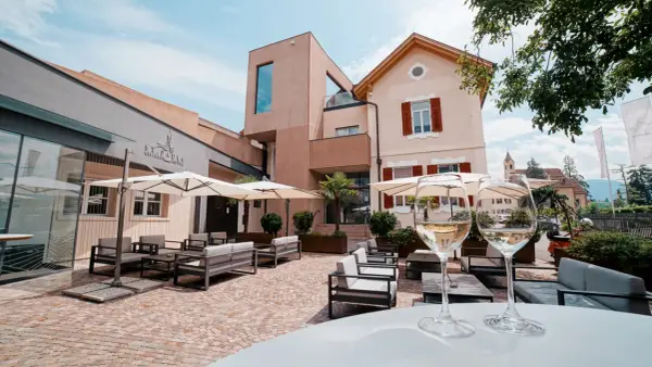 Terrazza accogliente con divani e ombrelloni, due calici di vino bianco in primo piano. La cantina St. Pauls sullo sfondo.